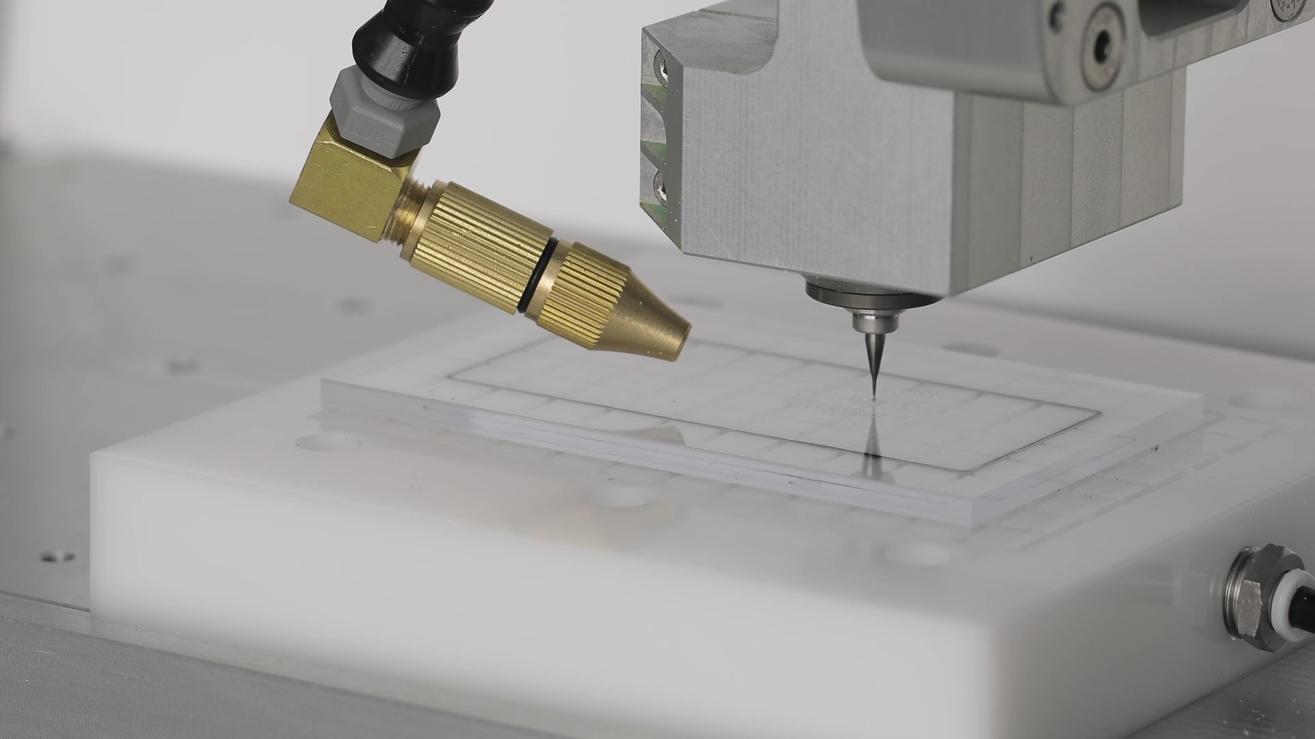 Micro cutting tool milling channels in a clear plate on a vacuum fixture, with the coolant nozzle aimed at the cut