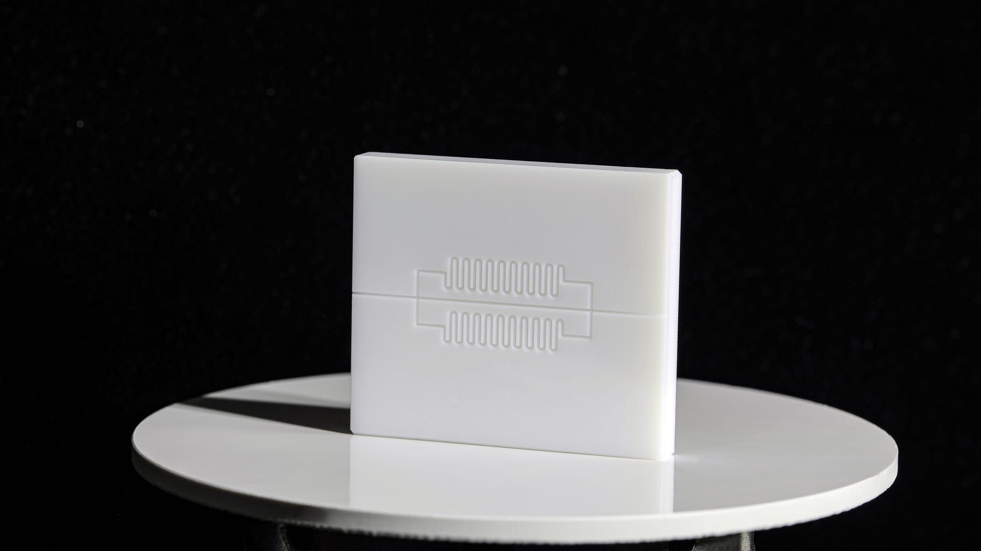 White plastic microfluidic chip with serpentine channels, standing on a display stand