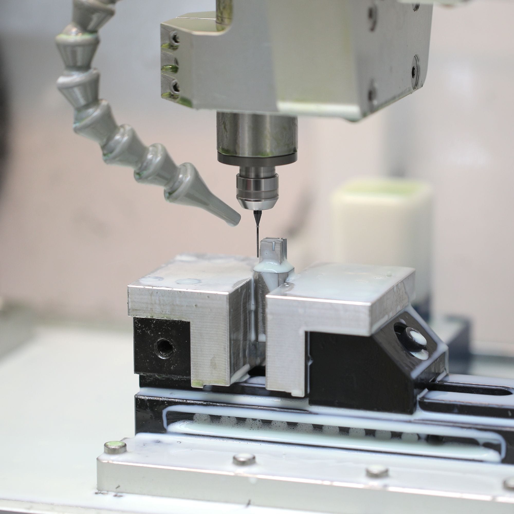 Milling a hard metal part held in a vise, with the coolant nozzle aimed at the cut