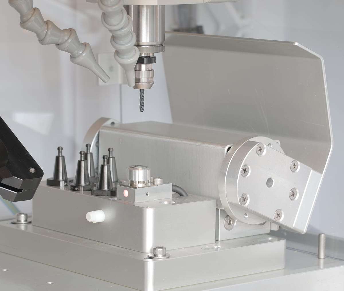 Automatic tool changer inside the Elara 2 work area: conical tool holders standing in their pots with the tool-length sensor beside them, the spindle and coolant nozzles above