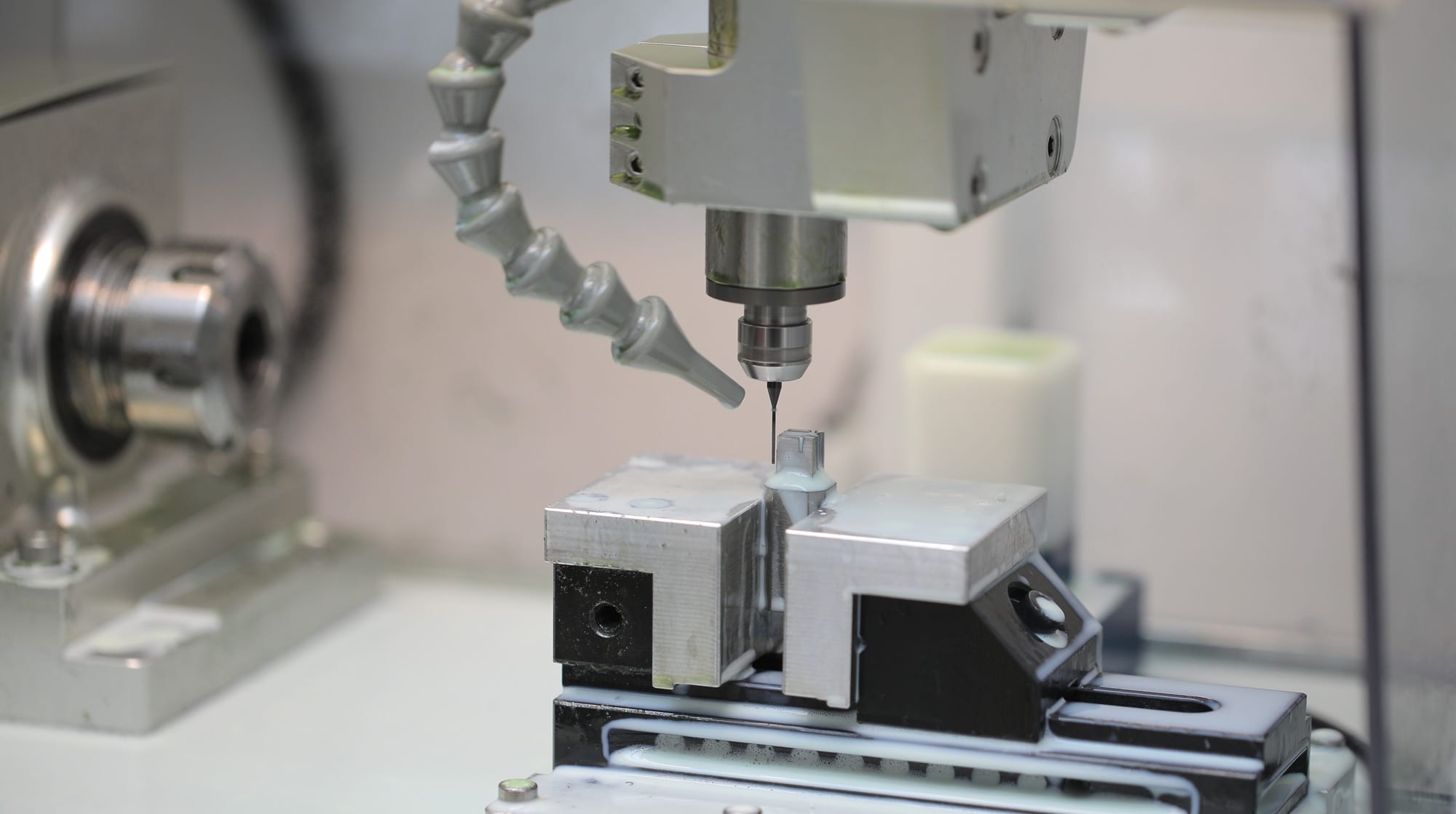 Nakanishi spindle nose at work: a small-diameter cutter machining a miniature part held in a machine vise, with the coolant nozzle at the cut