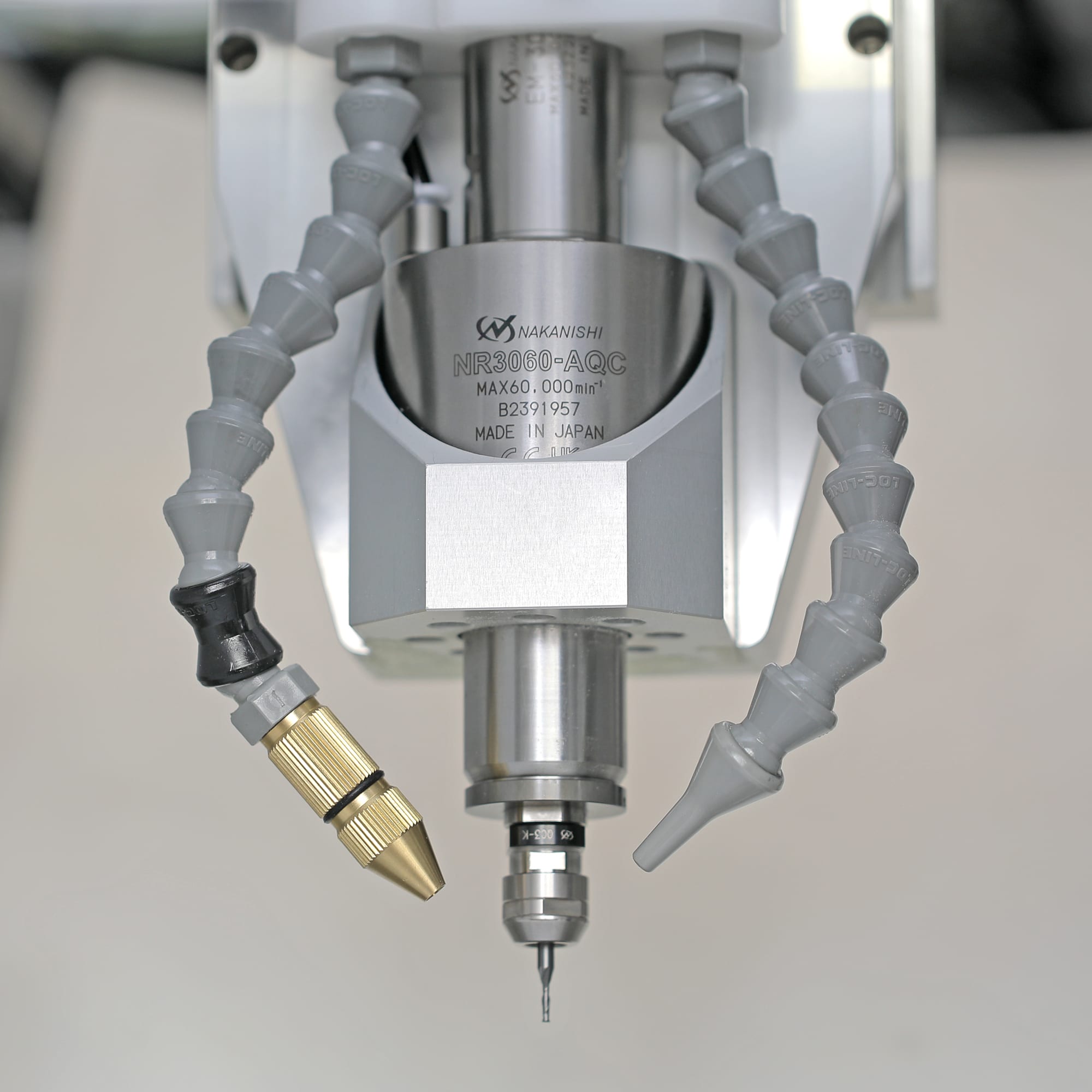 Nakanishi NR3060-AQC spindle nose close-up, engraved nameplate visible, dual coolant lines on either side, small drill bit in the collet