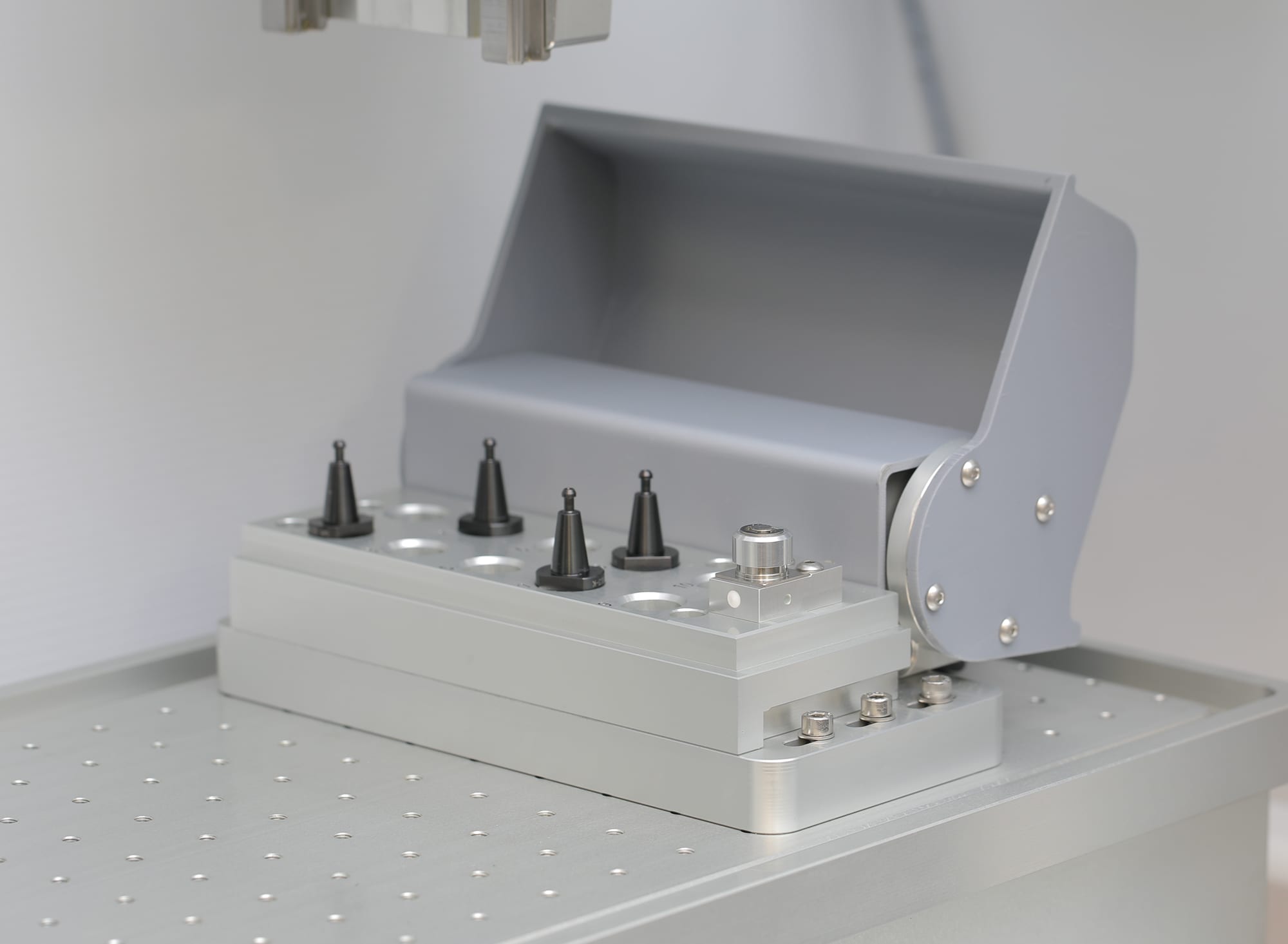 Automatic tool changer with the protective cover open, four conical tool holders seated in their pots and the tool-length sensor block beside them